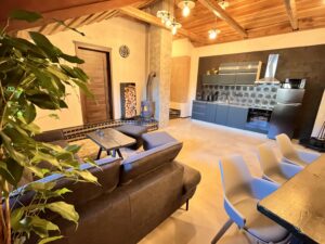 Interiér prostorného obývacího pokoje s tmavou kuchyňskou linkou, dřevěným stropem a krbovými kamny.