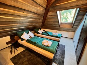 Podkrovní ložnice s dřevěným obložením stěn, dvěma oddělenými postelemi se zeleným povlečením a střešním oknem.